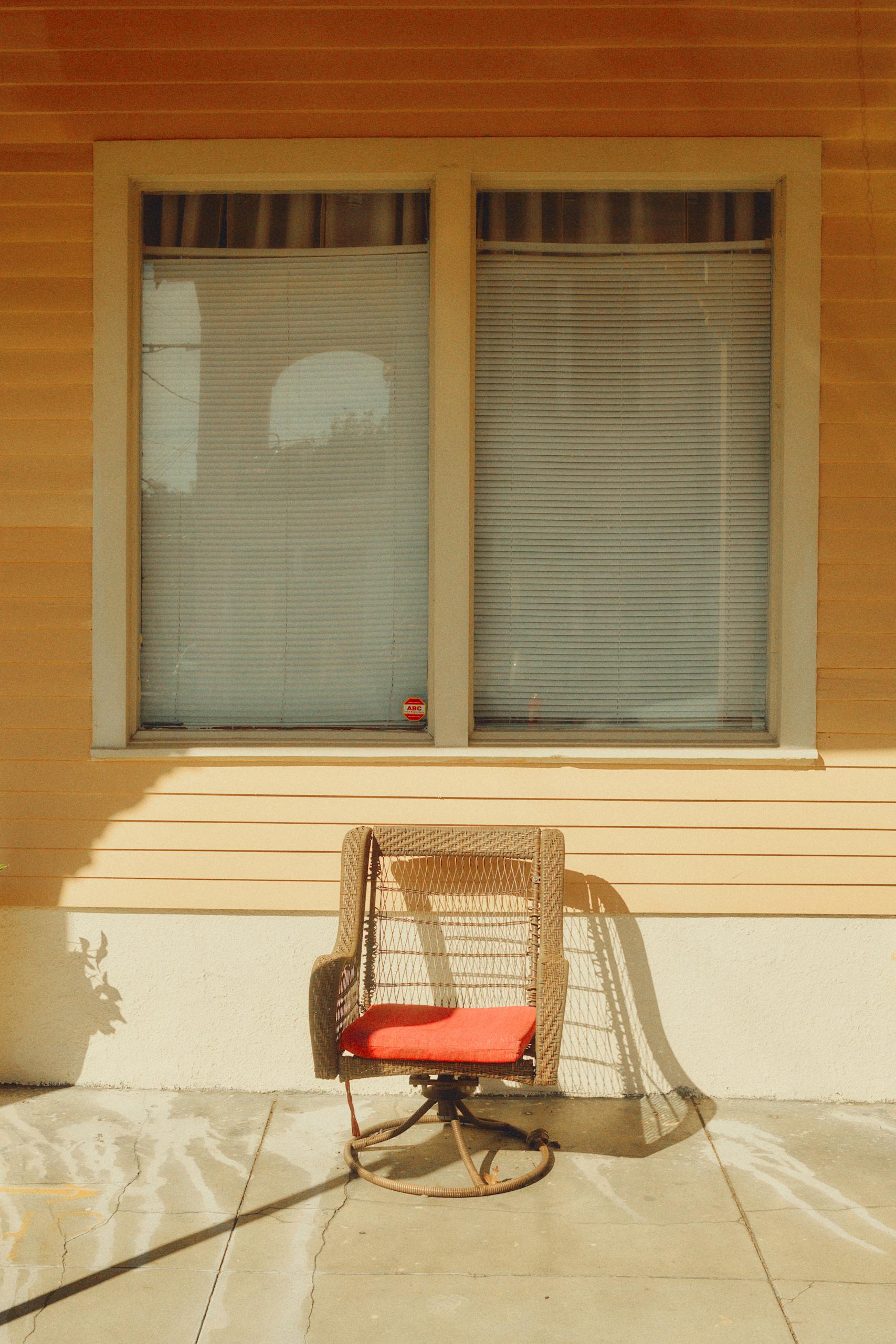 A wicker chair with a red cushion on a sunny New Orleans porch casting long shadows.